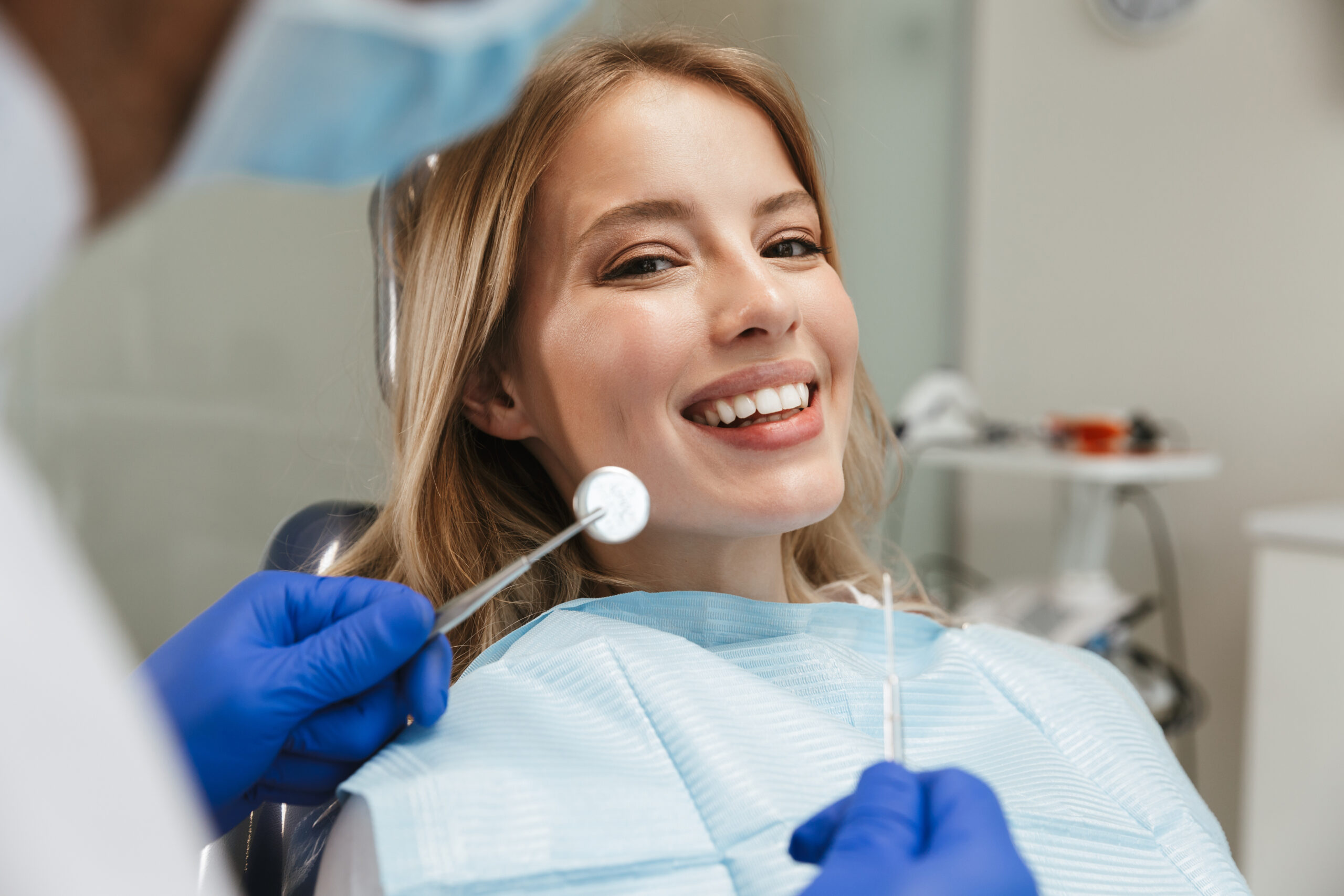 Image of beautiful young woman sitting in dental chair at medical center while professional doctor fixing her teeth
