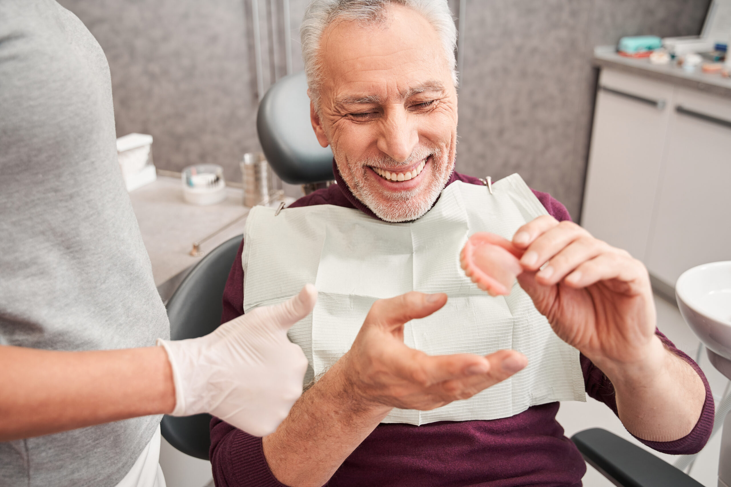 My new teeth. Cropped view of the dentist showing to senior grey haired patient teeth dentures while working at the dental clinic. Man sharing satisfaction smile